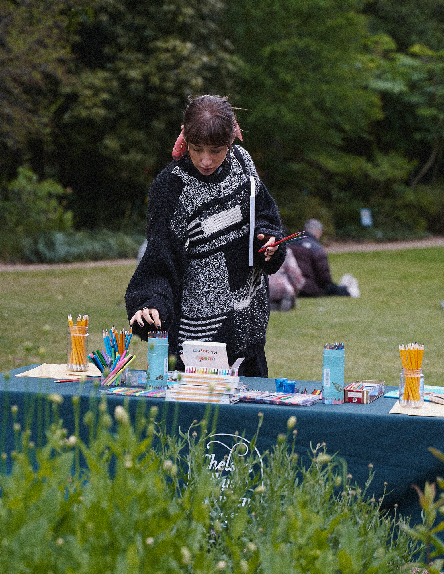 A person arranging coloured pencils and drawing materials on an outdoor table.