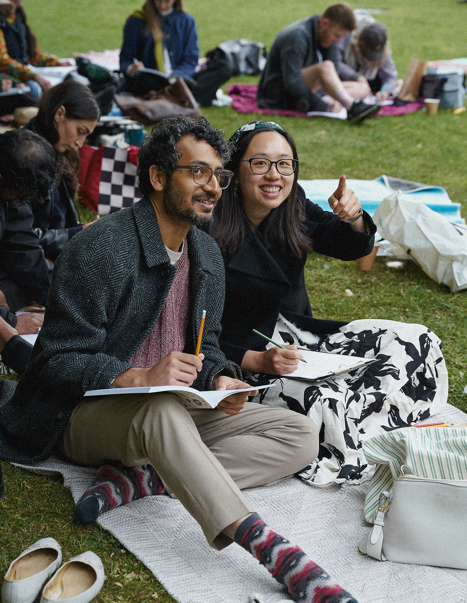 Two participants drawing in their books while seated on the Chelsea Physic Garden lawn.