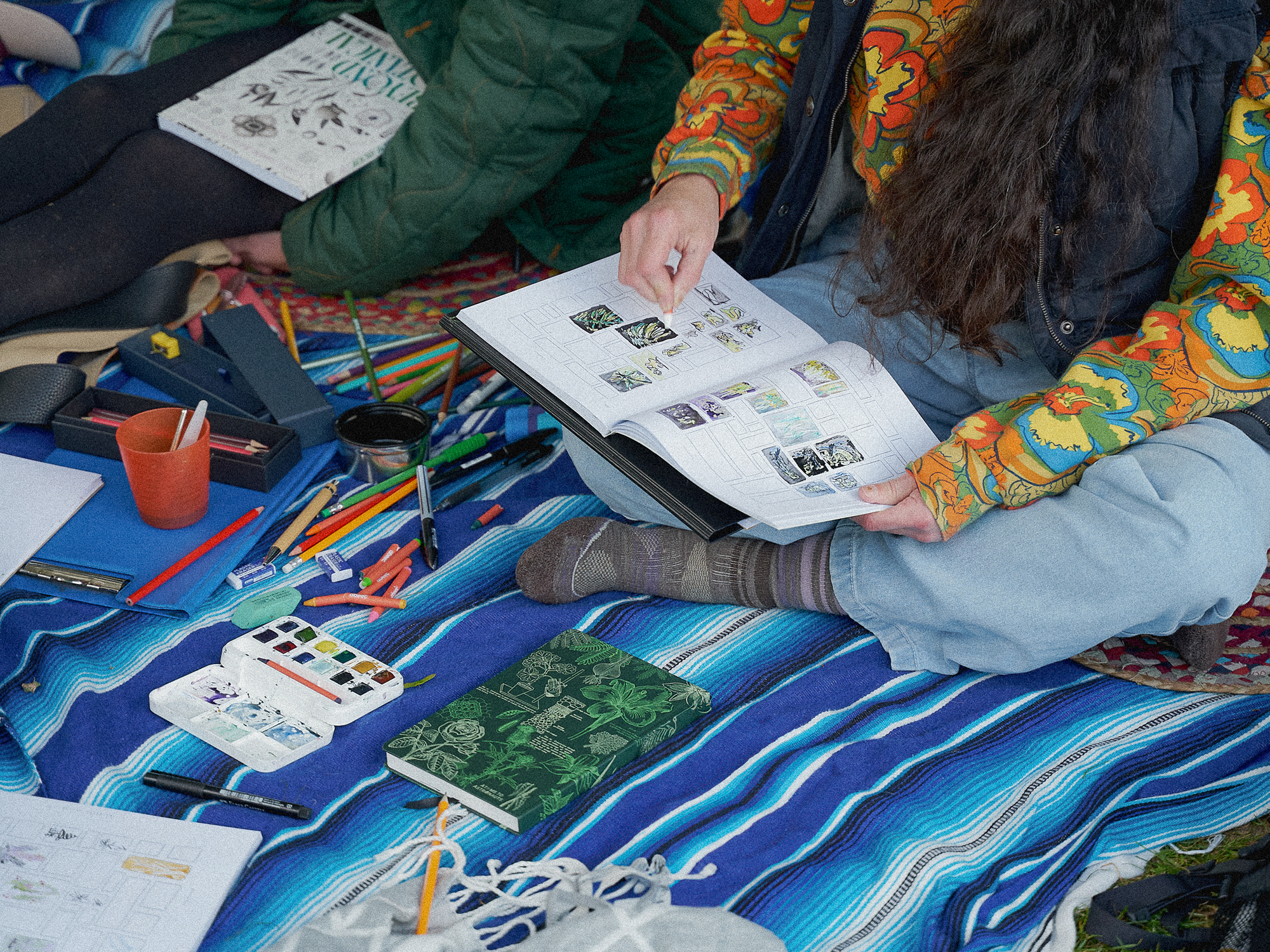 A participant adding coloured drawings to Beyond Botanical while seated on a blanket with art materials.