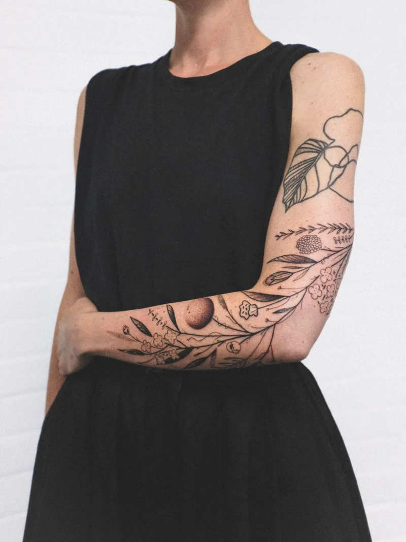 Detail view of a freehand botanical tattoo across the arms