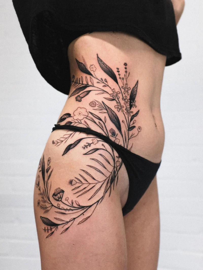 Freehand botanical tattoo across the legs and ribs