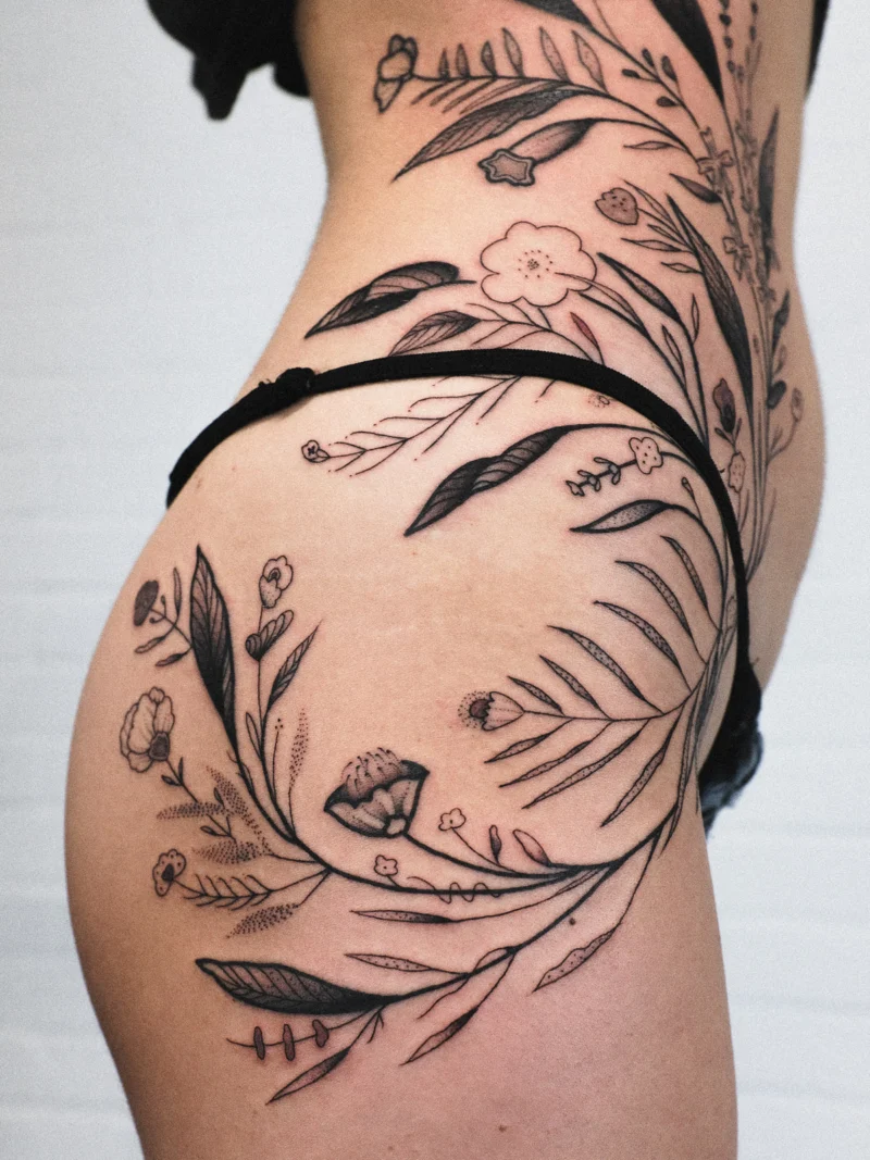 Another view of a freehand botanical tattoo across the legs and ribs