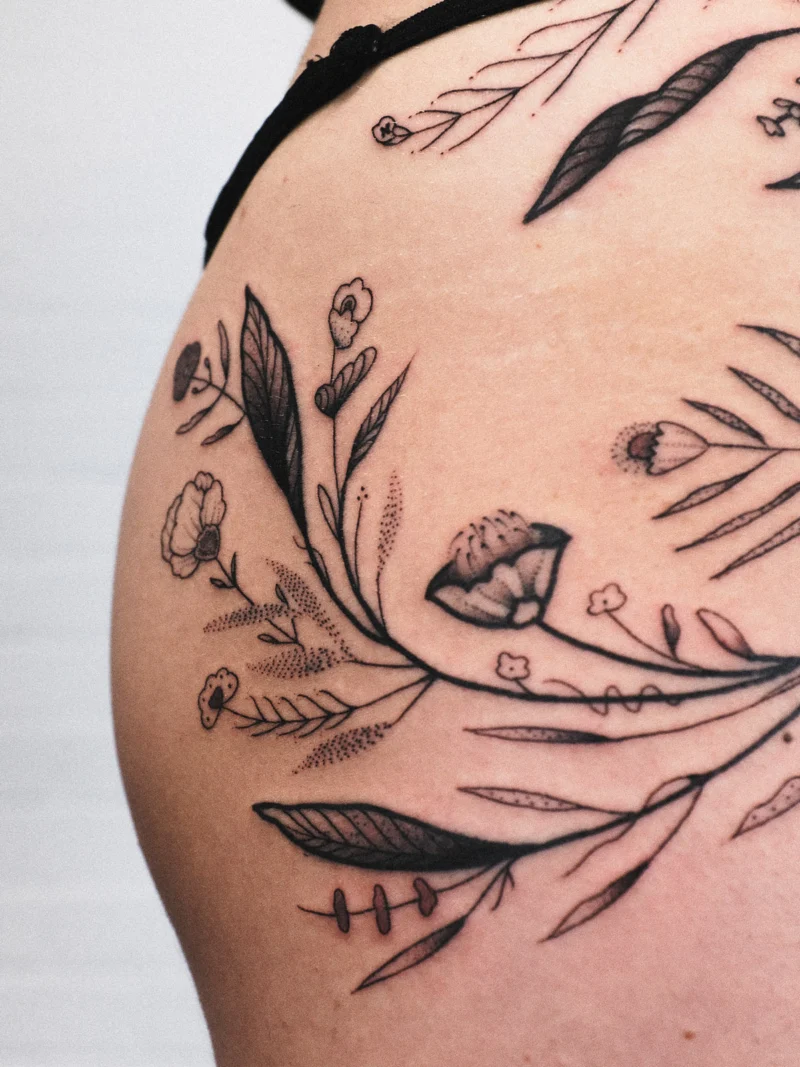 Detail view of a freehand botanical tattoo across the legs and ribs