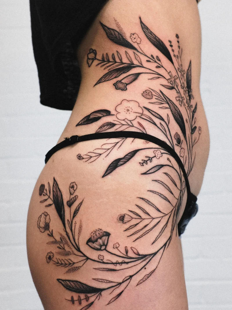 Detail view of a freehand botanical tattoo across the legs and ribs