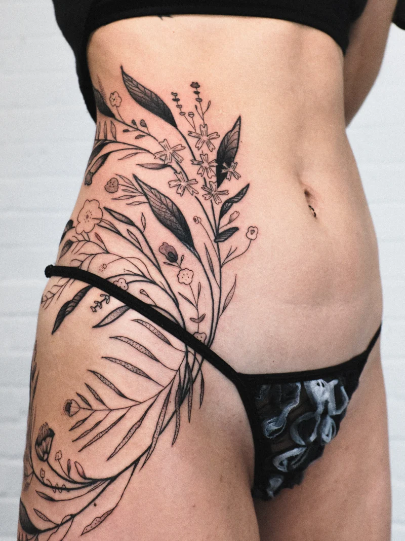 Detail view of a freehand botanical tattoo across the legs and ribs