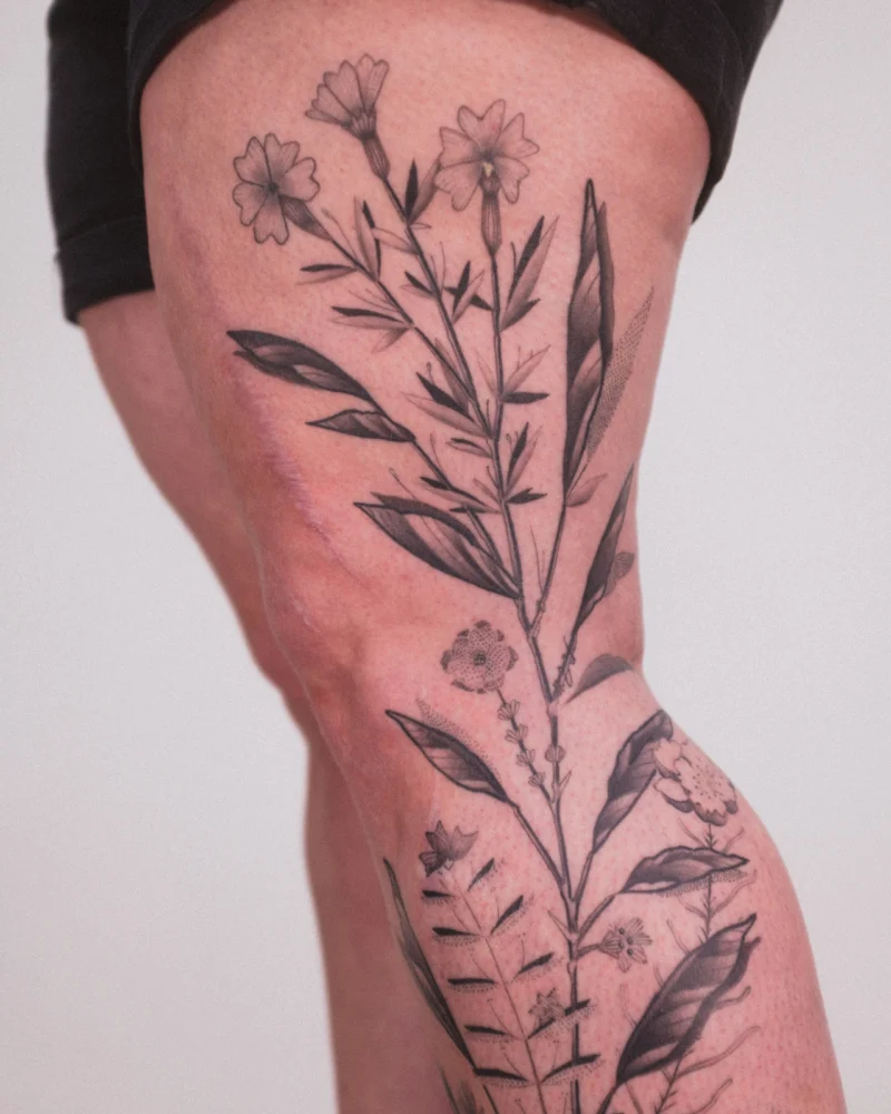 Detail view of a freehand botanical tattoo across the legs