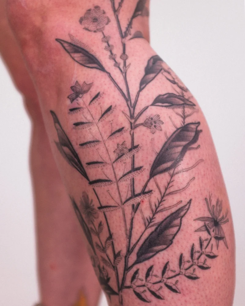 Detail view of a freehand botanical tattoo across the legs