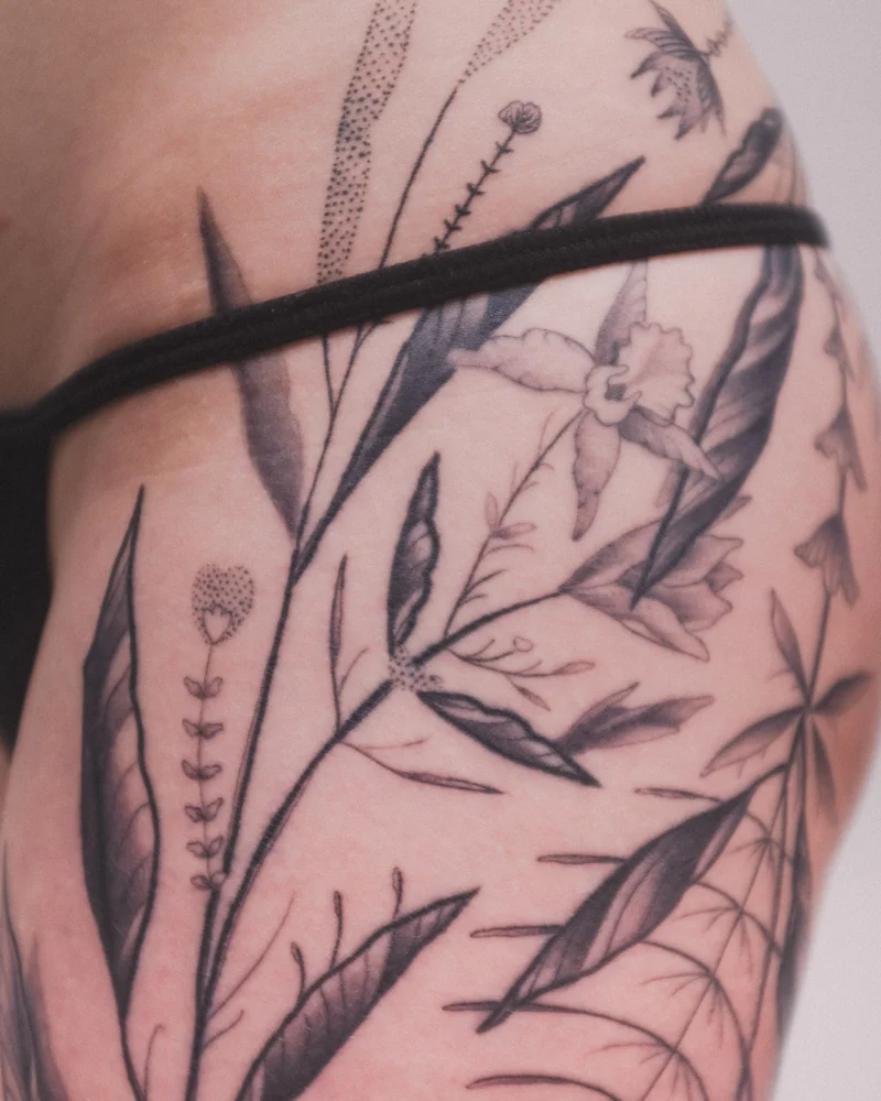 Detail view of a freehand botanical tattoo across the legs