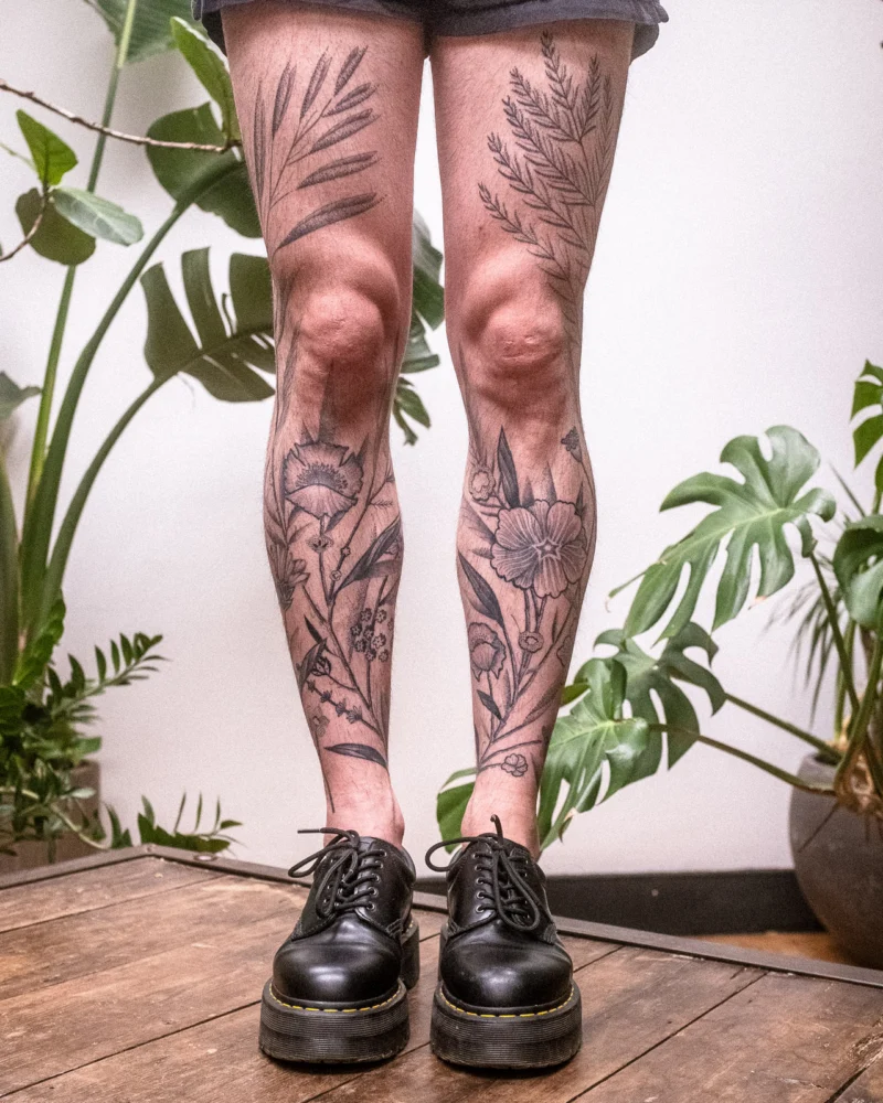 Detail view of a freehand botanical tattoo across the legs