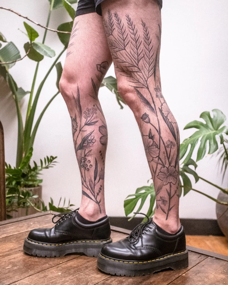 Detail view of a freehand botanical tattoo across the legs