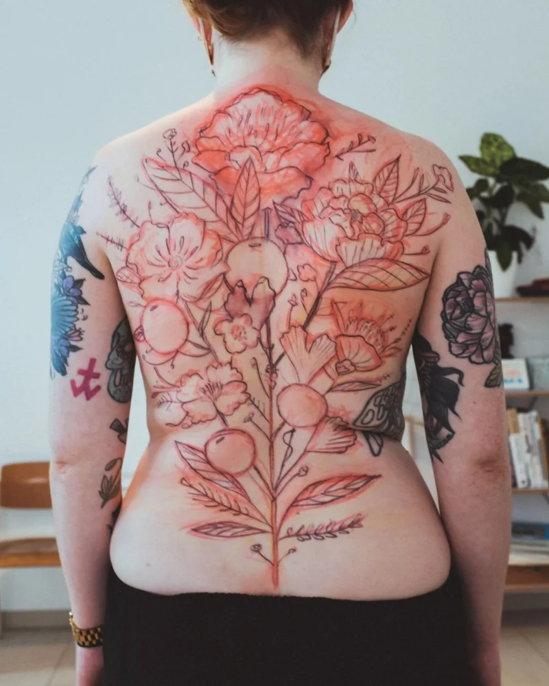 A red freehand botanical guide drawing across a client’s back before tattooing.