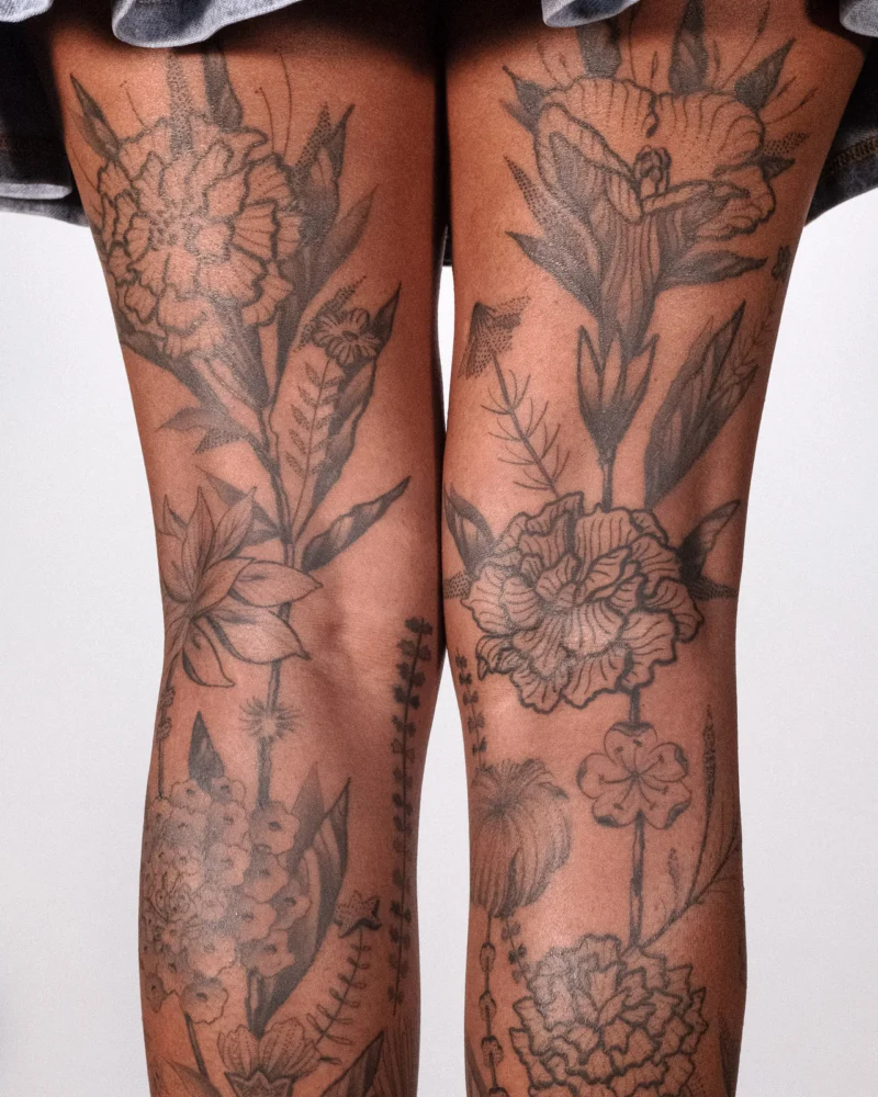 Paired black botanical tattoos extending across both legs on dark skin.