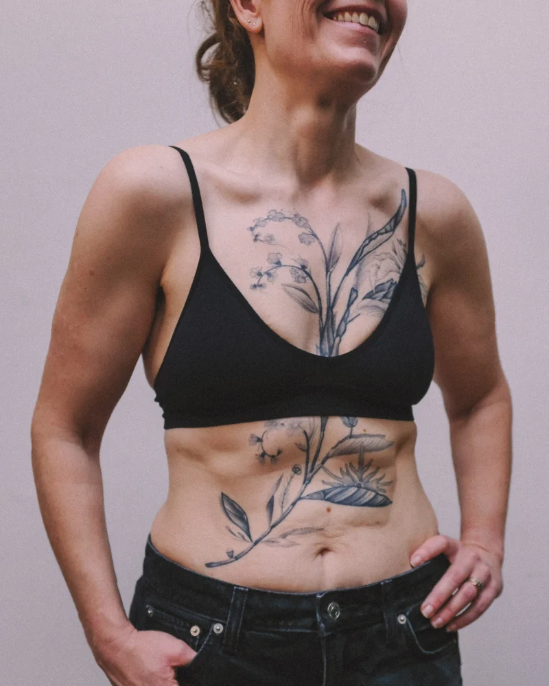 A black botanical tattoo extending from the chest across the torso.