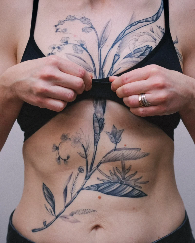 Botanical tattoo with a large flower and stems extending across the chest and abdomen